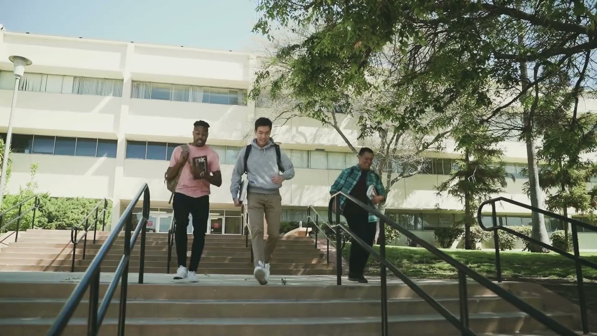 Three college students walk down the steps of a campus building.